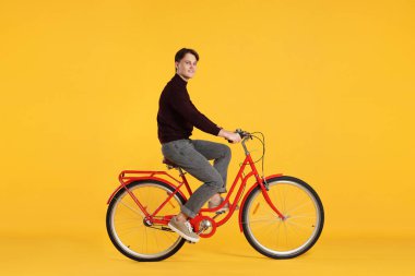 Turuncu arka planda kırmızı bisiklet süren yakışıklı bir adam.