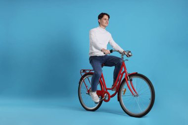 Açık mavi arka planda kırmızı bisiklete binen yakışıklı adam, metin için boşluk