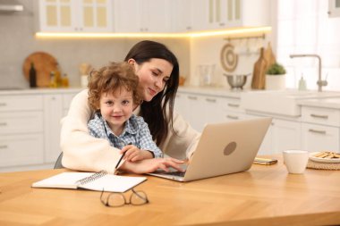 Laptop 'la çalışan bir kadın ve oğlu ofis odasındaki ahşap masada çalışıyor.