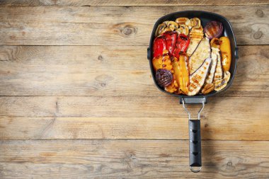 Ahşap masada tavada lezzetli ızgara sebzeler ve mantarlar, üst manzara. Metin için boşluk