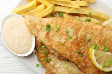 Beyaz ahşap masada soslu, limonlu ve yeşil soğanlı İngiliz Geleneksel Balık ve patates kızartması.