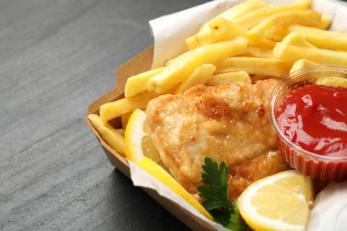 Sos, limon ve maydanozlu İngiliz Geleneksel Balık ve patates kızartması siyah desenli masada, yakın plan.