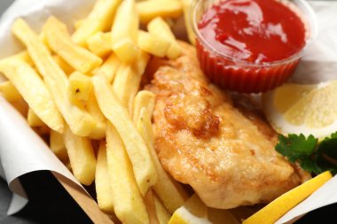 İngiliz Geleneksel Balık ve patates kızartması soslu, limonlu ve maydanozlu kağıt kutuda, yakın plan.