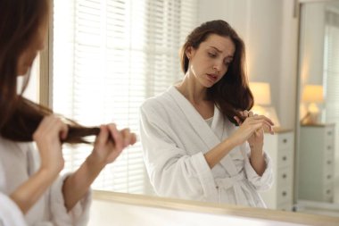 Saç dökülme sorunu olan kadın aynaya bakıyor.