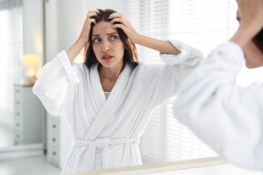 Saç dökülme sorunu olan kadın aynaya bakıyor.
