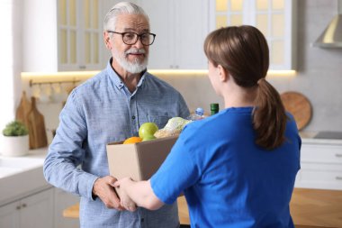 Yaşlılar için insani yardım. Gönüllü, içinde yiyecek olan karton kutuları evin içindeki yaşlı adama veriyor.