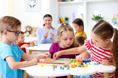 İlkokulda ders sırasında beyaz masada oturan sevimli çocuklar ve öğretmenler.