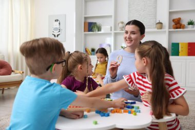 İlkokulda ders sırasında beyaz masada sevimli çocuklar ve gülümseyen öğretmen.