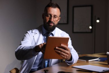 Doktor, gece vardiyası sırasında klinikte tablet üzerinde çalışıyor.