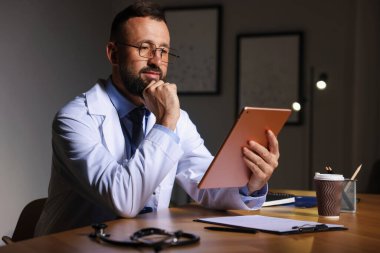 Doktor, gece vardiyası sırasında klinikte tablet üzerinde çalışıyor.