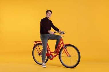 Turuncu arka planda kırmızı bisiklet süren yakışıklı bir adam.