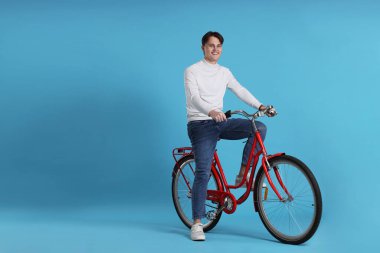 Açık mavi arka planda kırmızı bisiklete binen yakışıklı adam, metin için boşluk