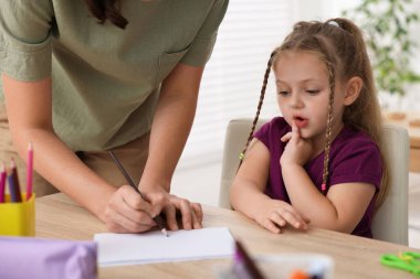 Öğretmen ve küçük kız ilkokulda ahşap masada, yakın çekim.