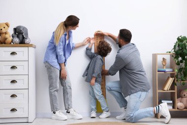 Ebeveynler, evlerinde beyaz duvarın yanında küçük oğullarının boyunu ölçüyorlar.