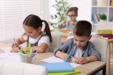İlkokulda sanat dersi sırasında ahşap masada oturan çocuklar.
