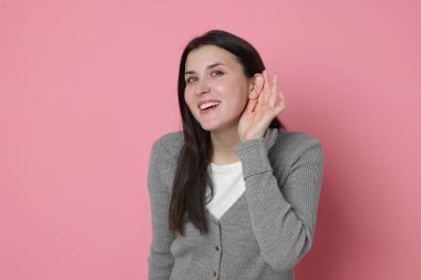 Gülümseyen kadın pembe arka planda el ele hareketler gösteriyor.