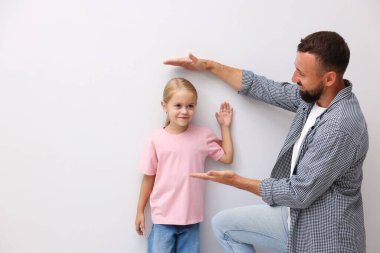 Babası, evdeki beyaz duvarın yanında küçük kızının boyunu ölçüyor.