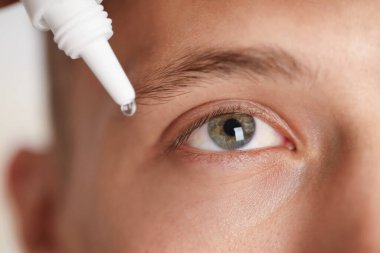 Işık arkaplanına göz damlası uygulayan adam, yakın plan