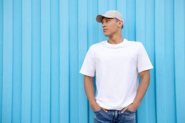 Açık mavi duvarın yanında beyaz tişört giyen genç bir adam. Tasarım için model