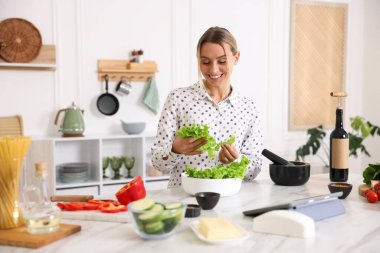 Yemek pişirme süreci. Mutfaktaki masada bir kase marulla gülümseyen kadın.