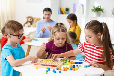 İlkokulda ders sırasında beyaz masada oturan sevimli çocuklar ve öğretmenler.