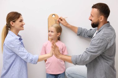 Küçük kızlarının boyunu ölçen ebeveynler beyaz duvarın yanında.