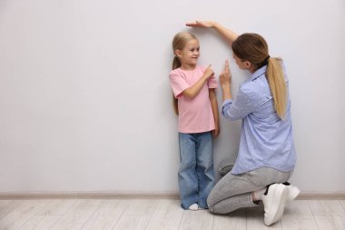 Anne, küçük kızının boyunu içeride beyaz bir duvarın yanında ölçüyor..