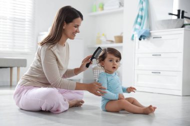 Anne banyoda bebeğinin saçını tarıyor.