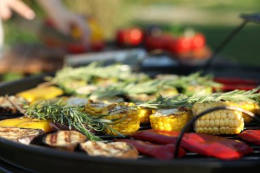 Vejetaryen barbeküsü. Dışarıdaki masada ürünleri kesen kadın, pişmiş sebzelerle ızgaraya odaklan.