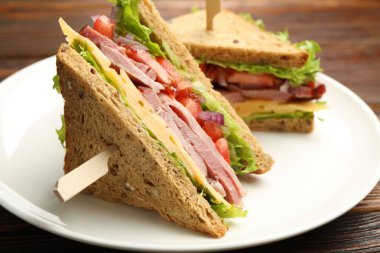 Delicious sandwiches with ham, cheese and vegetables on wooden table, closeup