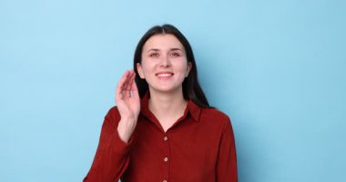 Gülümseyen kadın açık mavi arka planda el ele hareketler gösteriyor.