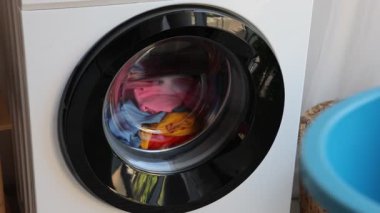 Çamaşır makinesinden çamaşırları çıkaran ve plastik havuza koyan kadın, yakın plan.