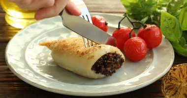 Ahşap masada mantarla doldurulmuş nefis ızgara kalamar kesen kadın, yakın plan.