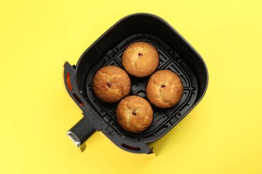 Air fryer basket with baked muffins on yellow background, top view