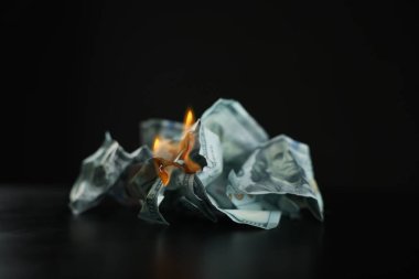 Burning dollar banknotes on black table against dark background