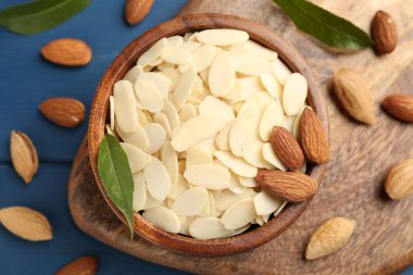 Fresh almond flakes, whole nuts and green leaves on blue wooden table, flat lay