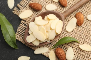 Fresh almond flakes, whole nuts and green leaves on grey table, above view