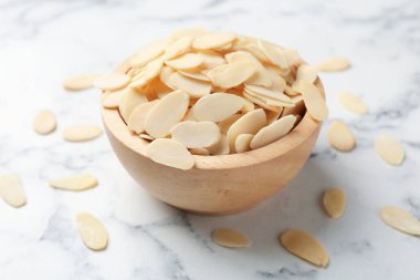Fresh almond flakes in bowl on white marble table, closeup