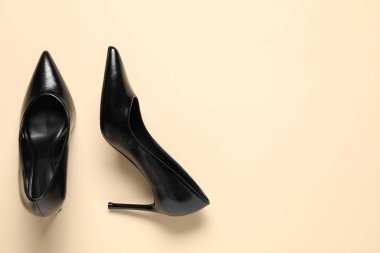 Pair of elegant black heels on beige background, top view with space for text. Stylish shoes