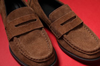 Pair of stylish brown shoes on red background, closeup