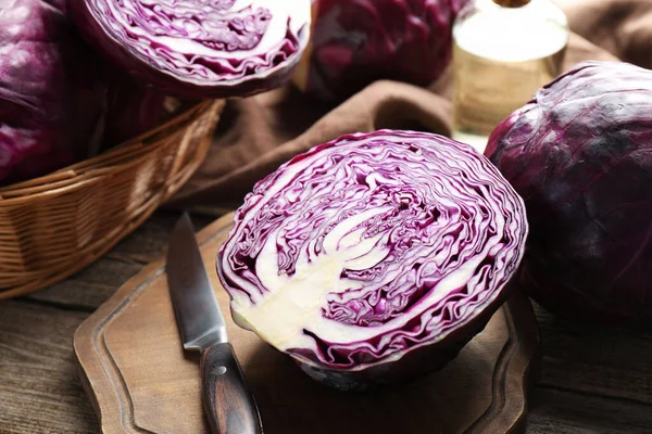 Fresh ripe red cabbages and knife on wooden table, closeup