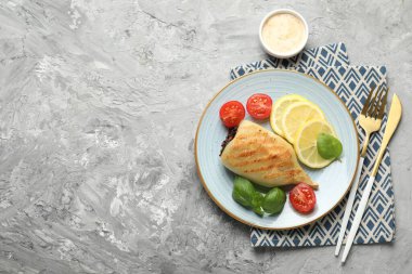 Piece of tasty grilled squid stuffed with mushrooms served with sauce on grey textured table, flat lay. Space for text