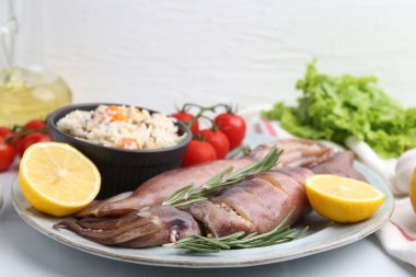 Çiğ mürekkep balıkları, dolma, biberiye, limon ve domatesler beyaz masada, yakın plan.