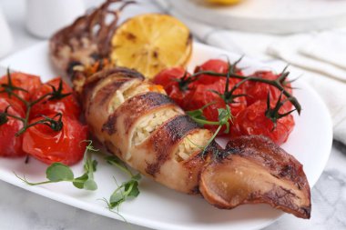 Tasty stuffed squid, microgreens, lemon and tomatoes on white marble table, closeup