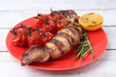 Lezzetli doldurulmuş mürekkep balığı, biberiye, limon ve domatesler açık ahşap masada, yakın plan.