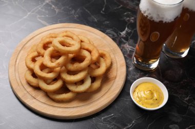 Siyah mermer masada servis edilen soslu ve biralı kızarmış kalamar halkaları, yakın plan.