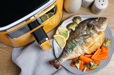 Pişmiş balık, biberiye, limon, sebze ve tava ahşap masada, düz yatıyordu.