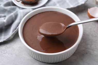 Gri masadaki kaşıkla kaseden çiğ çikolata hamuru alıyoruz. Yakın plan.