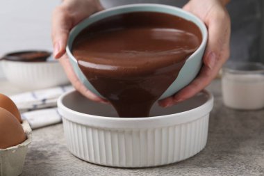 Gri masadaki pişirme kabına çiğ çikolata hamuru döken kadın.