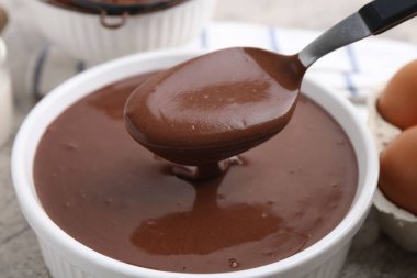 Gri masadaki kaşıkla kaseden çiğ çikolata hamuru alıyoruz. Yakın plan.